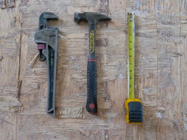 Pipe wrench, hammer and tape measure laid out on a timber bench